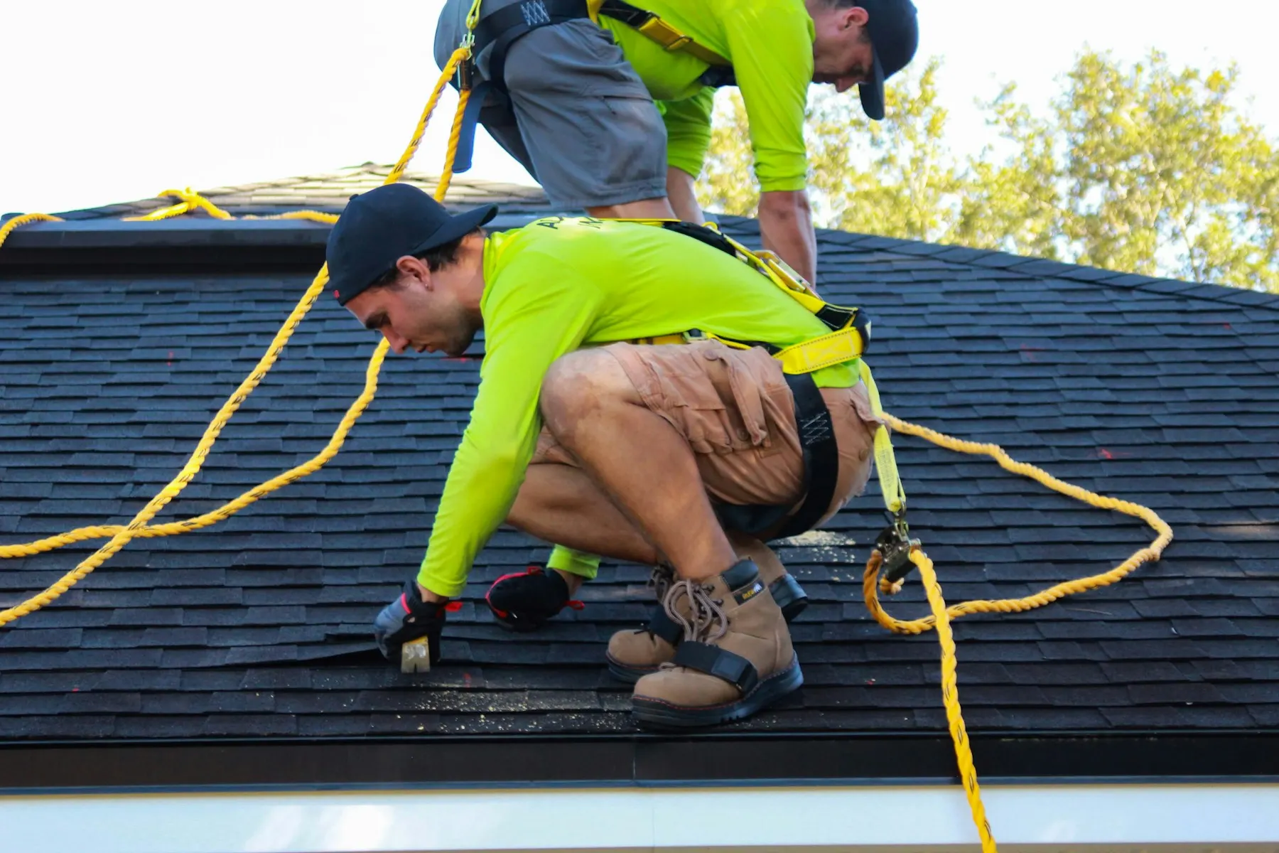 Two roofers in safety harnesses replacing damaged shingles