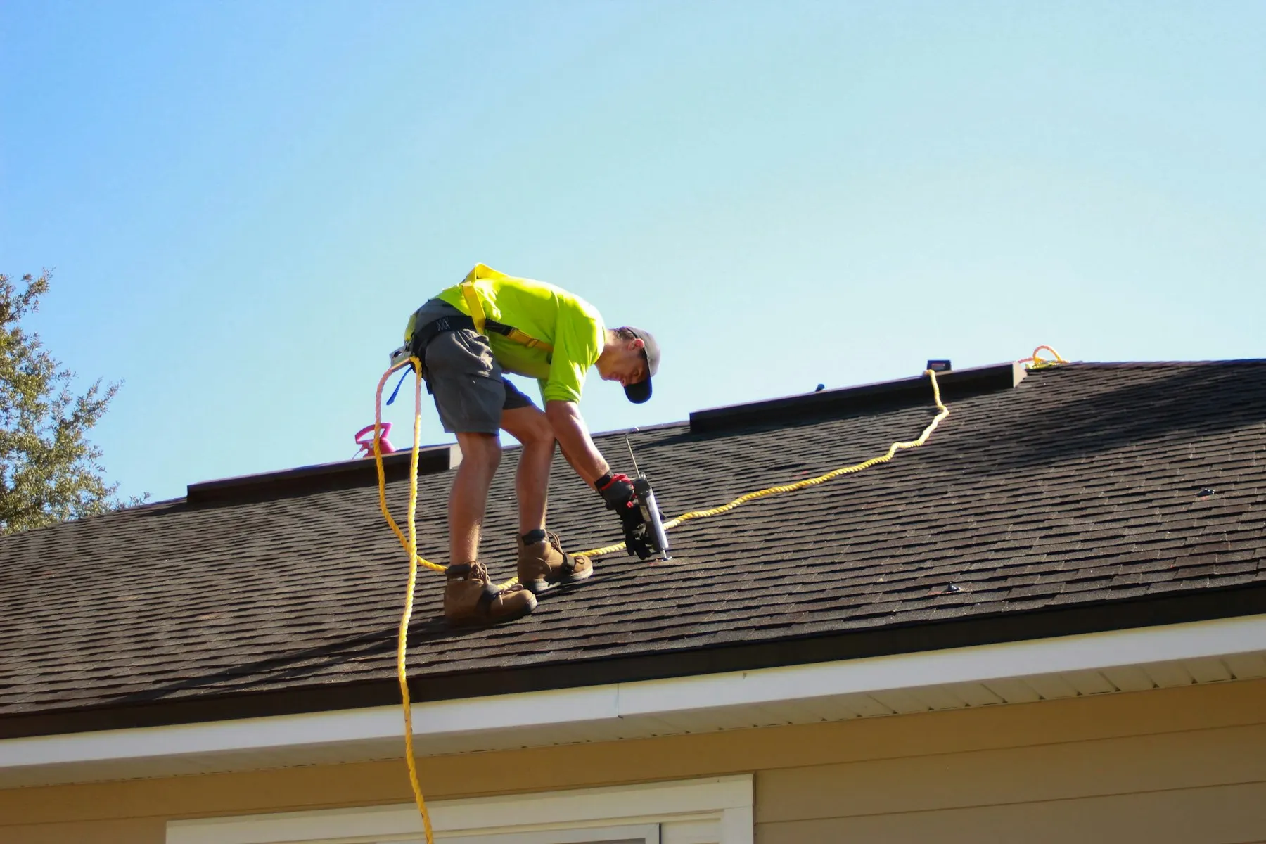 Roofer in a safety harness sealing a shingle roof