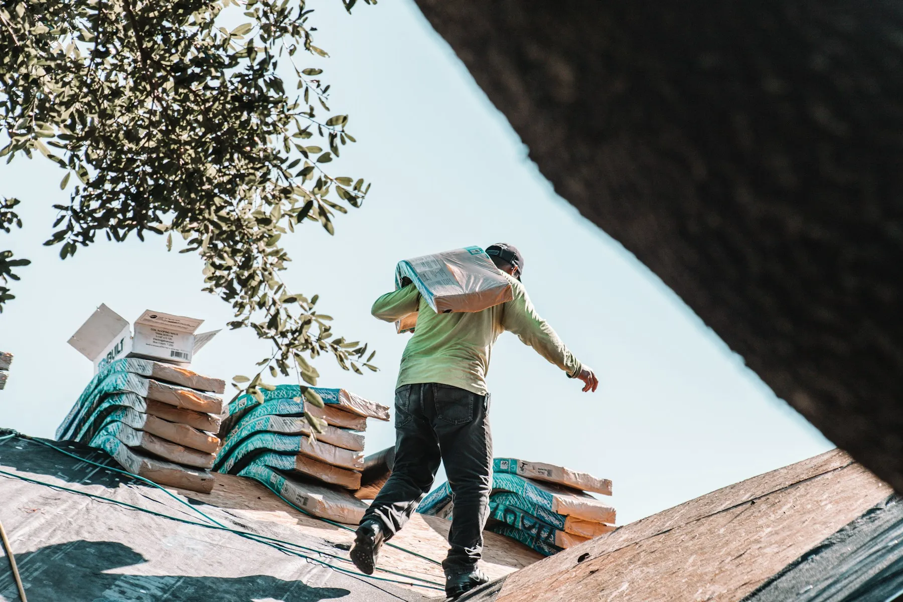 Roofer carrying a bundle of shingles across a roof deck during a replacement